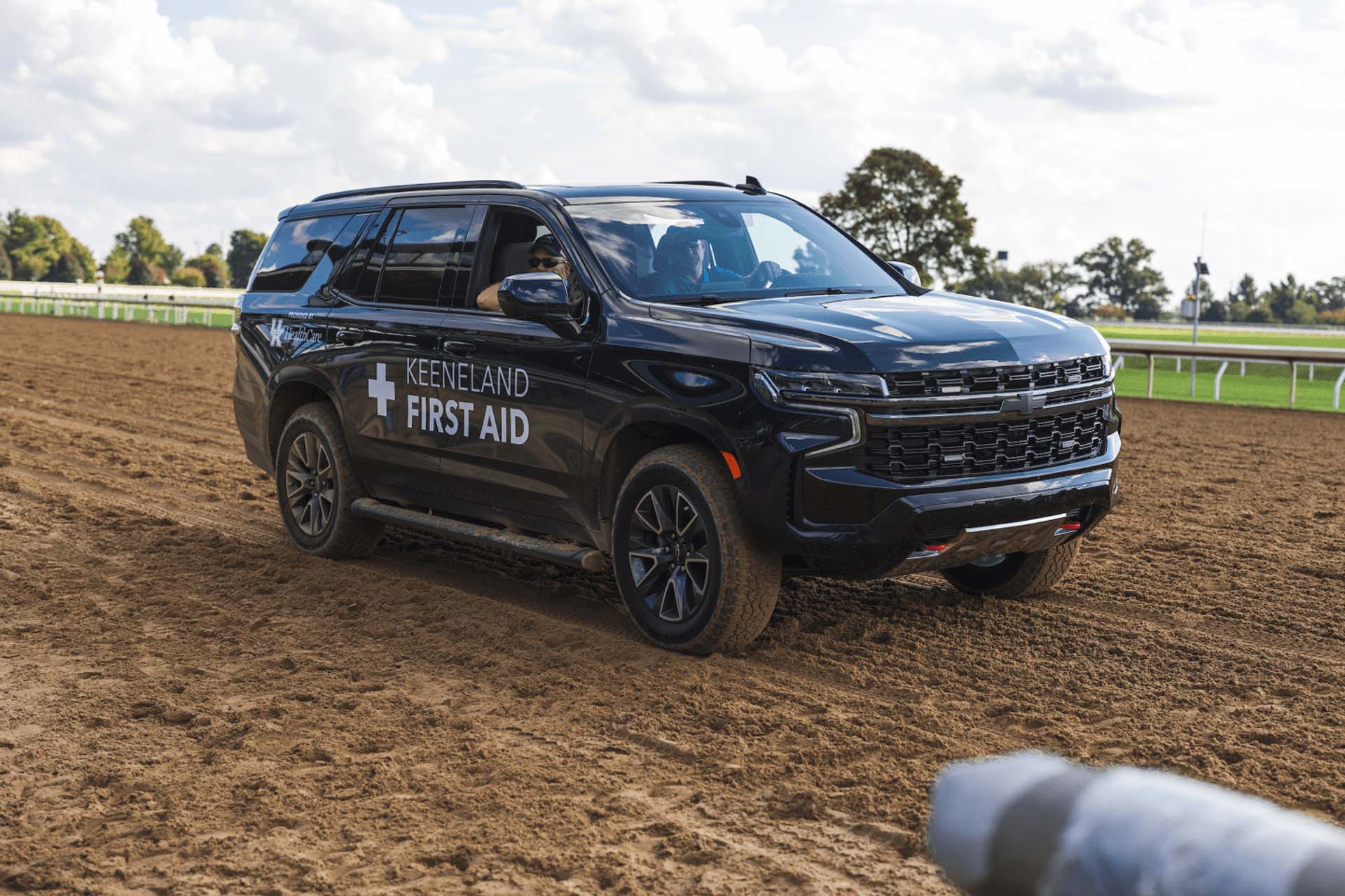 A picture of the Swiftjockey First Aid car on the dirt track. It is a large black Chevy SUV.